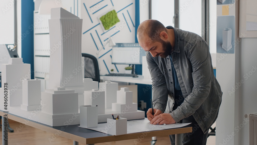 Poster man engineer analyzing building model to design blueprints plans on table. architect working with ma