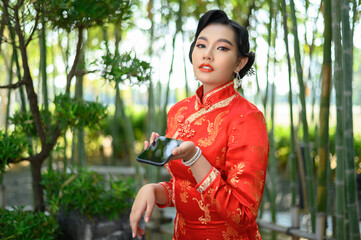 Asian pretty Chinese woman dress traditional cheongsam pose with mobile phone