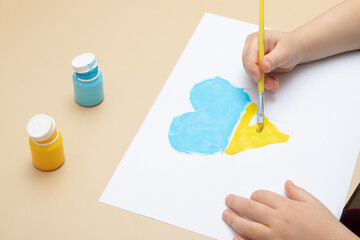 Yellow and blue paints and children's hands with a brush at the table. Drawings of Ukrainian children concept