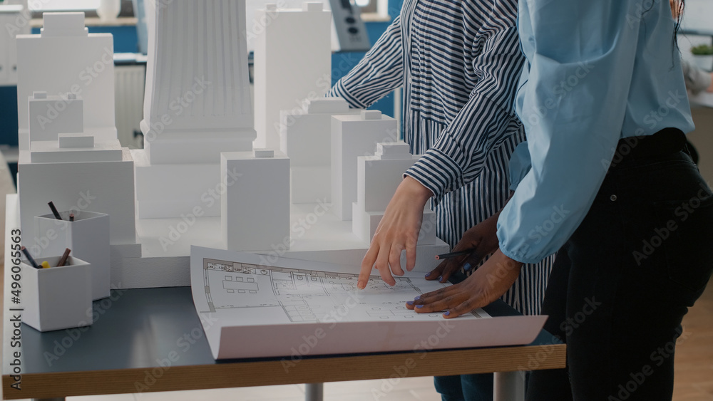 Poster close up of team of colleagues using blueprints plan to design urban construction on table. women ar