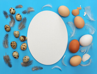 Set from chicken and quail eggs, feathers and shells on blue background .White frame-blank at the middle. . Free space for writing .Top view. Food or Easter concept.