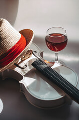 Romantic plot with a white violin and a glass red wine on a gray background, with a straw hat with a red piping