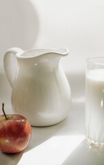 Delicate healthy theme with a glass of fresh milk, a snow-white jug and a yellow apple