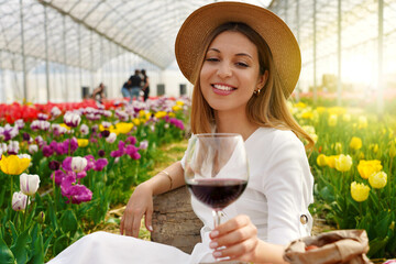 Relaxed beautiful woman enjoying a glass of red wine between tulips on spring time