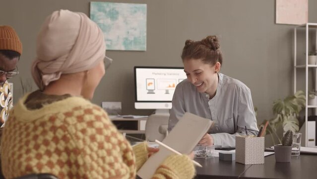 Slowmo of young diverse team of creative marketing specialists brainstorming ideas while having meeting at office table. One of women sitting in wheelchair