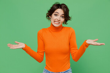 Young mistaken confused sad woman 20s wearing orange turtleneck spread hands shrugging shoulders...
