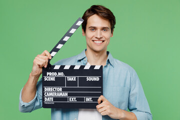 Cheerful happy charismatic excited jubilant exultant young brunet man 20s years old wears blue shirt holding classic black film making clapperboard isolated on plain green background studio portrait. - obrazy, fototapety, plakaty