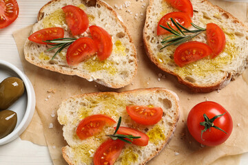 Tasty bruschettas with oil, tomatoes and rosemary on parchment paper, flat lay