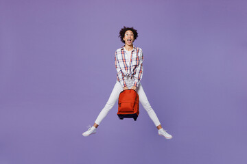 Full body happy young girl woman of African American ethnicity teen student in shirt hold backpack jump high with outstretched legs isolated on plain purple background. Education in college concept.