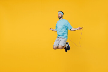 Fototapeta na wymiar Full body side view young fitness trainer instructor sporty man sportsman wearing headband blue t-shirt jump with skipping rope isolated on plain yellow background. Workout sport motivation concept.