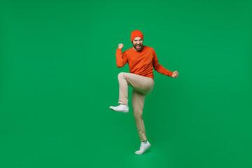 Full body young excited happy man 20s in orange sweatshirt hat doing winner gesture celebrate...