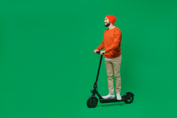 Full body side view young smiling happy fun cheerful caucasian man 20s wear orange sweatshirt hat riding electric scooter isolated on plain green background studio portrait. People lifestyle concept. © ViDi Studio