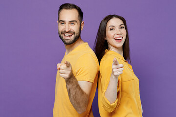 Fototapeta premium Young side profile view happy fun couple two friends family man woman together in yellow casual clothes stand back to back point index finger camera on you isolated on plain violet background studio.