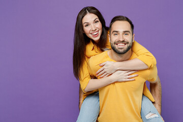 Fototapeta premium Young fun couple happy two friends family man woman together in yellow casual clothes looking camera giving piggyback ride to joyful, sit on back isolated on plain violet background studio portrait.