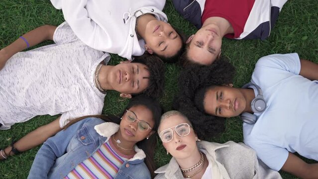 Relaxed teenager friends lying together on green grass with eyes closed, dreaming and sleeping. Group of young multi ethnic people