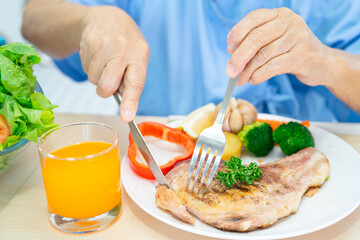 Asian senior or elderly old lady woman patient eating breakfast and vegetable healthy food with hope and happy while sitting and hungry on bed in hospital.
