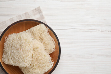 Bowl with dried rice noodles and napkin on white wooden table, top view. Space for text
