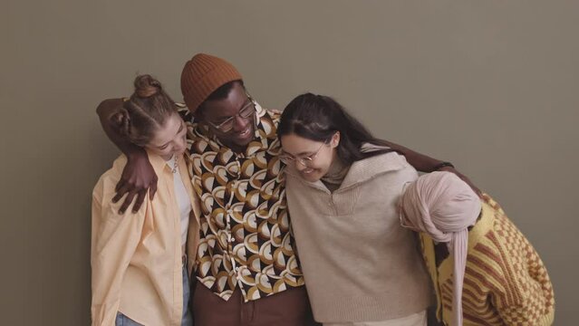 Medium slowmo portrait of diverse team of four young millennial friends smiling at camera standing against pastel olive green wall