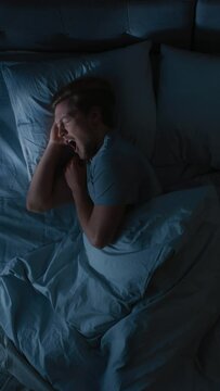Top View of Handsome Young Man Sleeping Cozily on a Bed in His Bedroom at Night. Video Footage with Vertical Screen Orientation