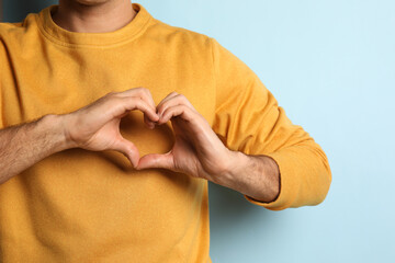 Man making heart with hands on light blue background, closeup