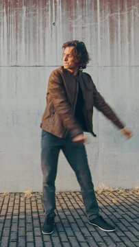 Cheerful and Happy Young Man with Long Hair Actively Dancing While Walking Down the Stairs. He's Wearing a Brown Leather Jacket. Vertical Screen Orientation Video