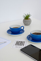 QR code for online menu service at table in restaurant New contactless technology lifestyle protect. Phone and blue mugs on the table
