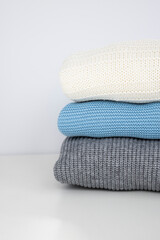 A stack of neatly folded warm knitwear wool on a white table Capsule wardrobe clothing storage