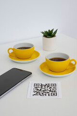 QR code for online menu service at table in restaurant New contactless technology lifestyle protect. Phone and yellow mugs on the table