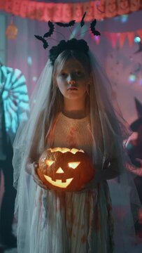Halloween Costume Party: Little Girl in a Bloody White Bride Dress Holding Scary Pumpkin Head with Candle Inside. Vertical Screen Orientation Video