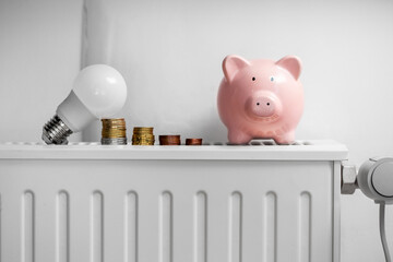 heating, energy crisis and consumption concept - piggy bank, light bulb and money on radiator at home