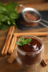 Glass of delicious hot chocolate with fresh mint and cinnamon sticks on wooden table