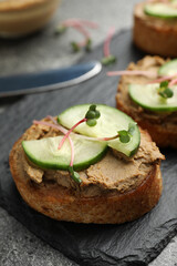 Slices of bread with delicious pate, cucumber and microgreens on grey table, closeup