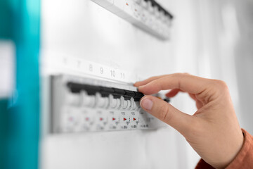 electricity, energy and power consumption concept - close up of hand switching electric board at home