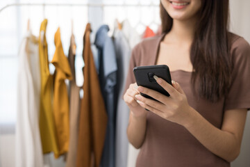 Young beautiful asian woman business owner at fashion store using smartphone check stock on rails clothing standing and smile. Asian female entrepreneur working in clothes shop.