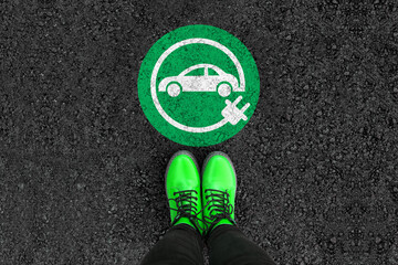 a woman with a boots is standing next to electric car sign on road asphalt 