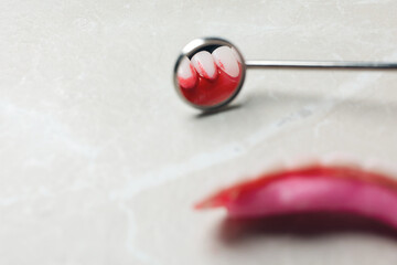 Dental mirror near gum model with blood on light grey table, closeup. Space for text