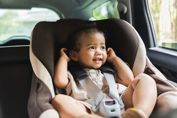 Asian Baby Toddler girl sitting in car seat and looking through window. Infant baby with safety belt in vehicle. Safety car. Family travel concept