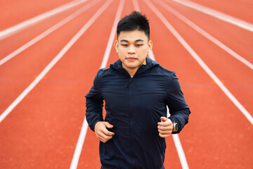 Attractive Young chinese man wearing sportswear running on track at sport stadium. Fit man jogging...