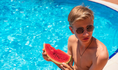 happy teenager with a slice of watermelon in his hands is relaxing by the pool.