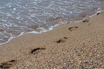 Footprints of a man on the yellow beach sand from walking barefoot by the sea with water that washes away the footprints.