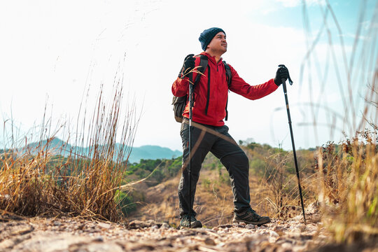 Young asian man mountaineering wearing jacket walking at outdoor. Tourist on top of the mountain walking by trekking pole. Travel adventure hiking concept.
