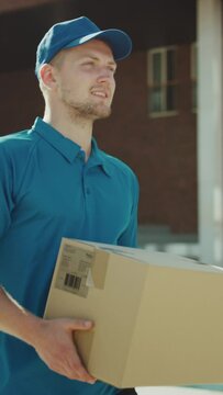 Handsome Delivery Man Holds Cardboard Box Package Walks Through Modern Stylish Business District. Low Angle Slow Motion. Vertical Screen Orientation Video