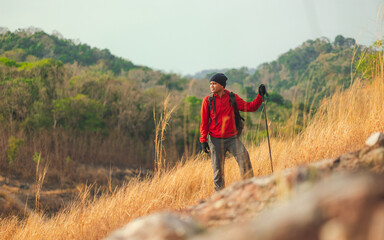 Young asian man mountaineering wearing jacket walking at outdoor. Tourist on top of the mountain walking by trekking pole. Travel adventure hiking concept.