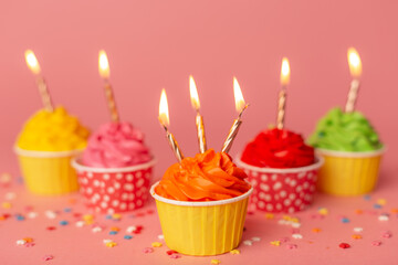 A colorful birthday cupcakes with candle on the pink background. Birthday cupcakes