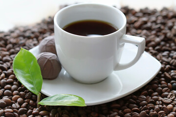 White cup of coffee with chocolate candy close up on coffee beand background