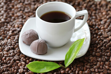 White cup of coffee with chocolate candy close up on coffee beand background