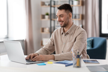 Obraz premium distance education, school and remote job concept - happy smiling male teacher or student with laptop working or learning at home office