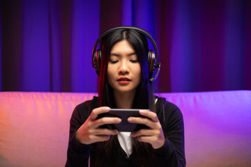 Playing video game on cellphone. Young asian pretty woman sitting on sofa holding smartphone in...