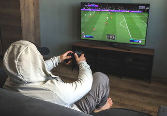 Guy playing a video game console. Game is football. Back view. Selective focus