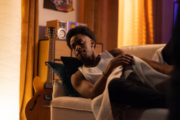 Fototapeta premium A man wakes up in the morning at sunrise in the living room on the couch, pulls the blanket off himself, looks at his watch, gets out of bed, overslept for work